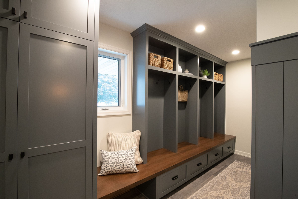 Gray locker-style storage with built-in bench, drawers, and baskets. Neutral walls and accent pillows.
