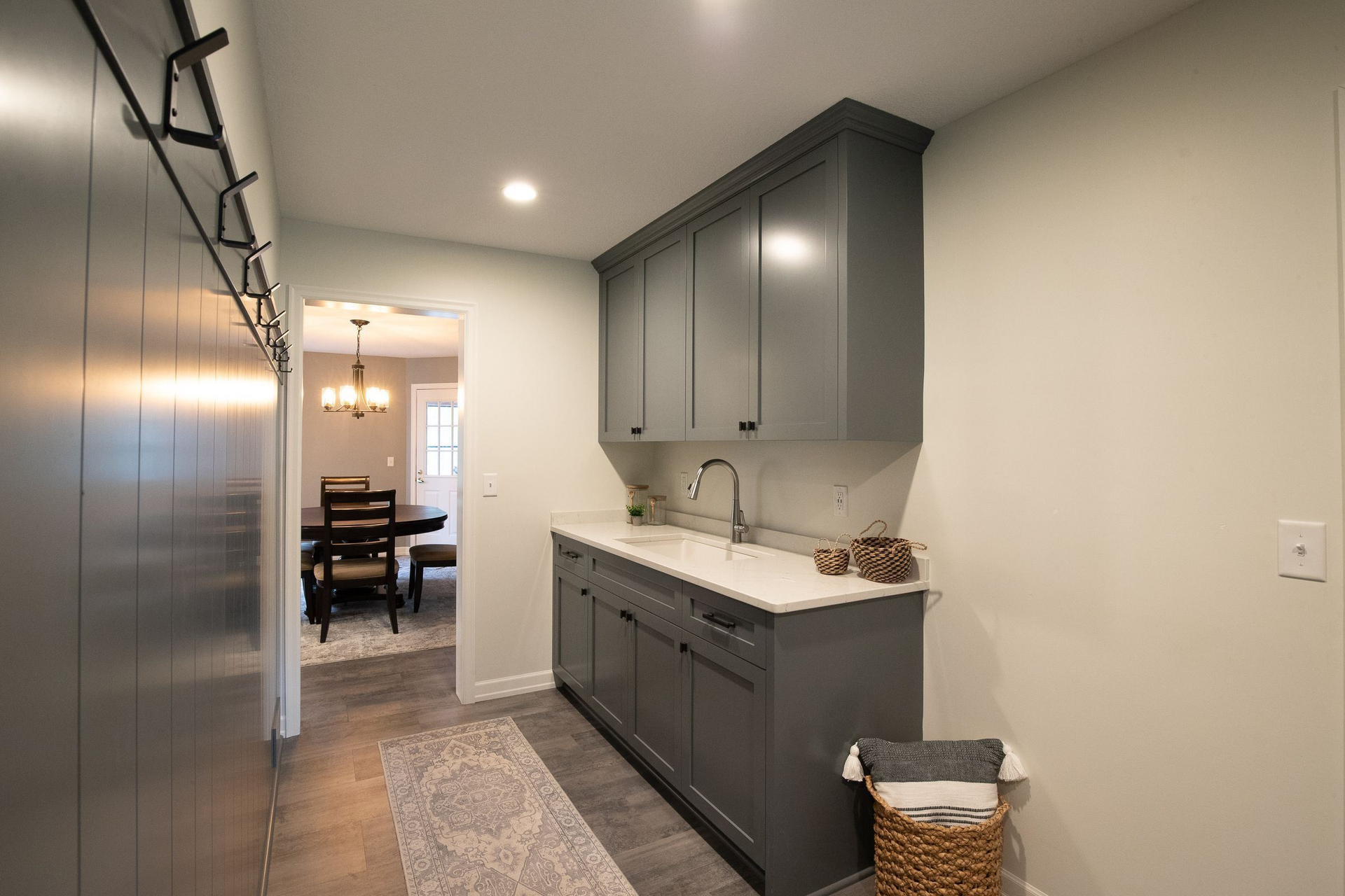Gray laundry room with cabinetry, sink, and rug. Doorway leads to dining area.