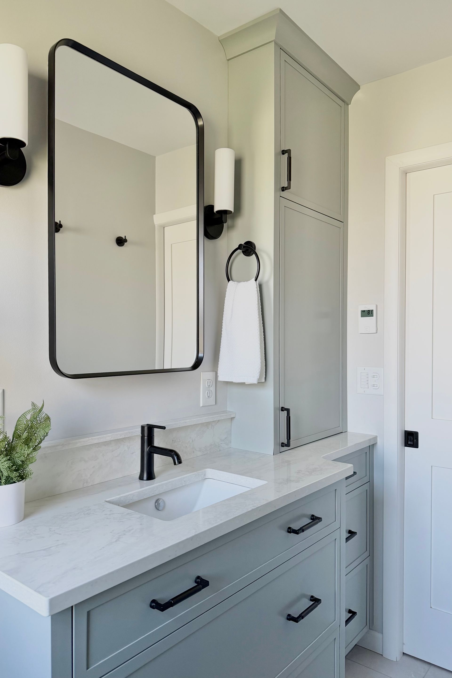 Modern bathroom vanity with large mirror, black fixtures, marble countertop, and built-in cabinet storage.