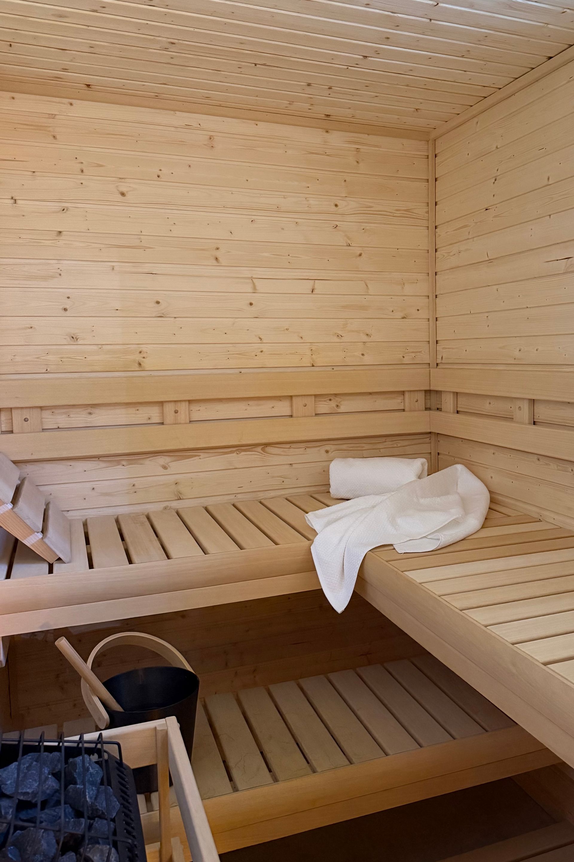 Wooden sauna interior with benches, a towel, and a bucket on the floor in bathroom.