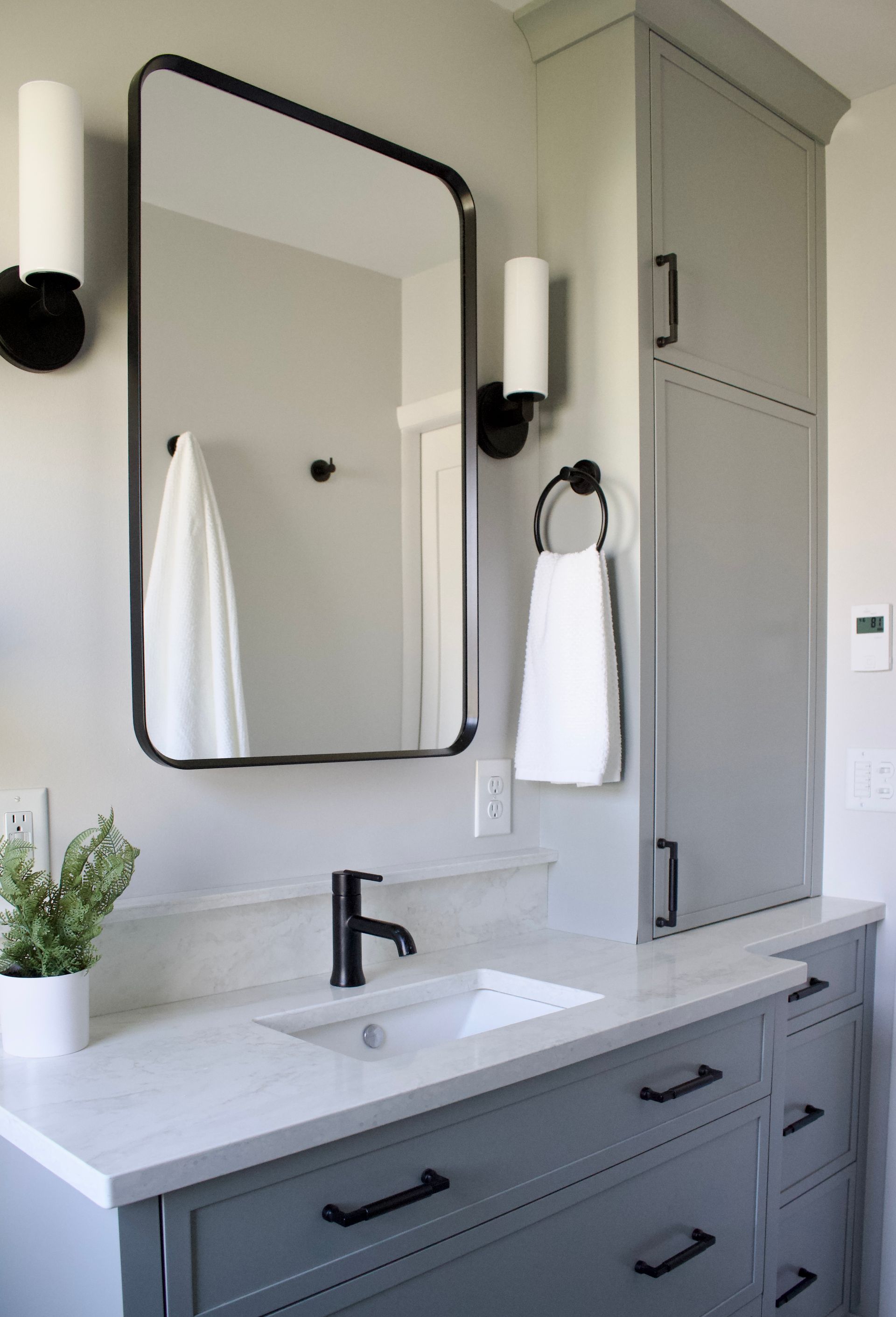 Modern bathroom vanity with black faucet, rectangular mirror, wall sconces, and built-in linen cabinet