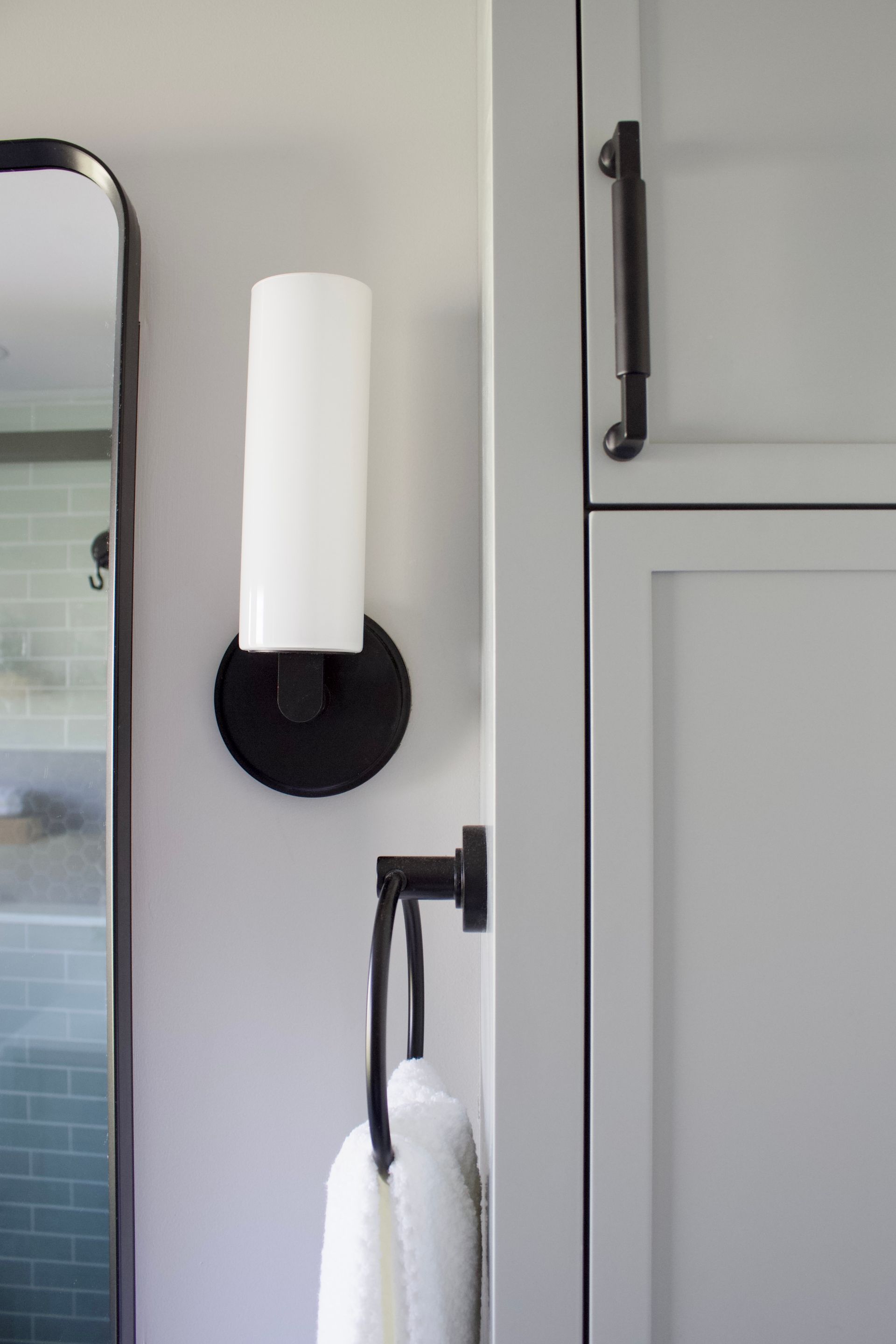 Bathroom vanity with black wall sconce, mirror edge, and white towel on a rack.