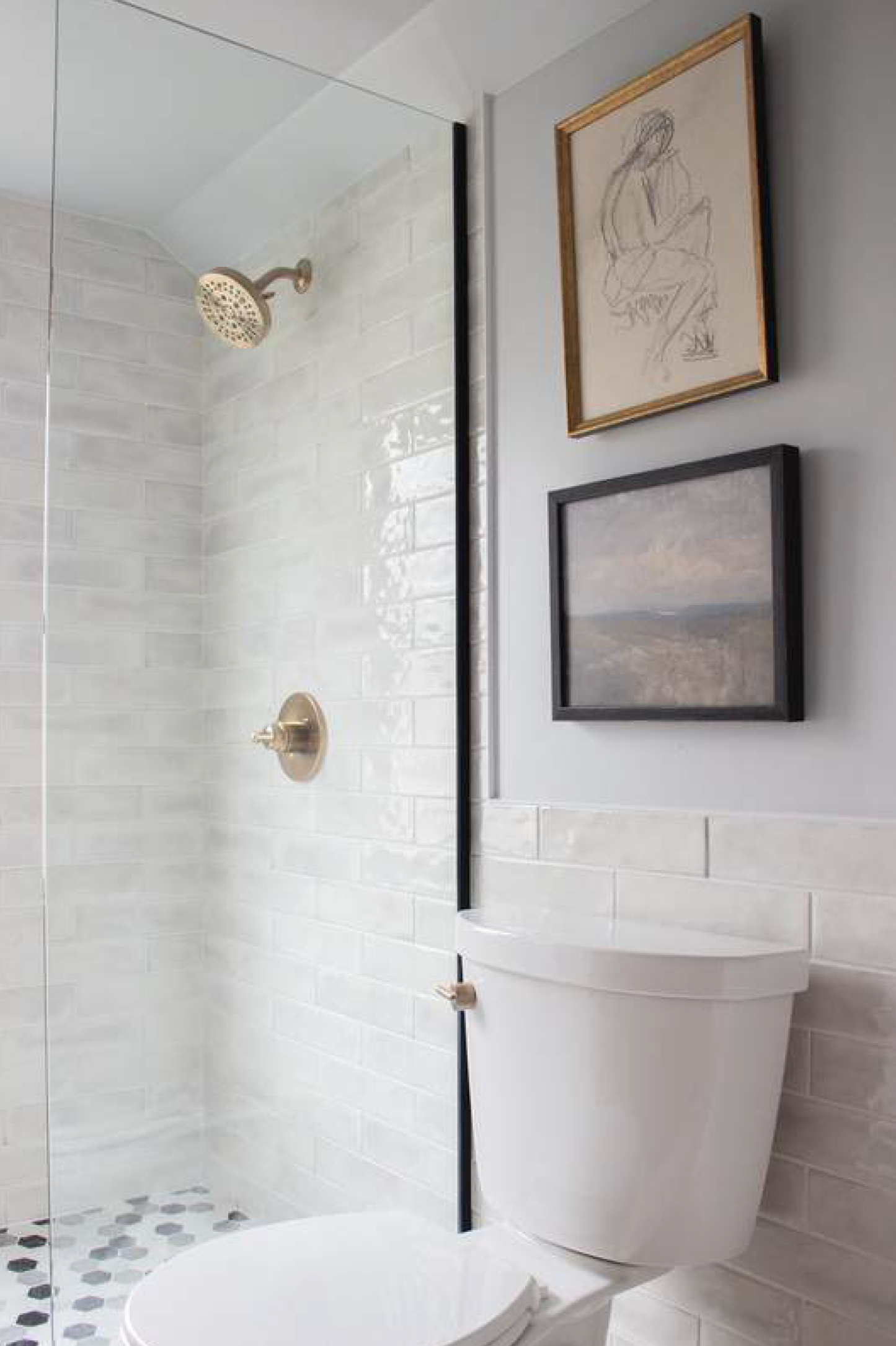 Bathroom with white tile shower, toilet, gold fixtures, and two framed pictures on a gray wall.