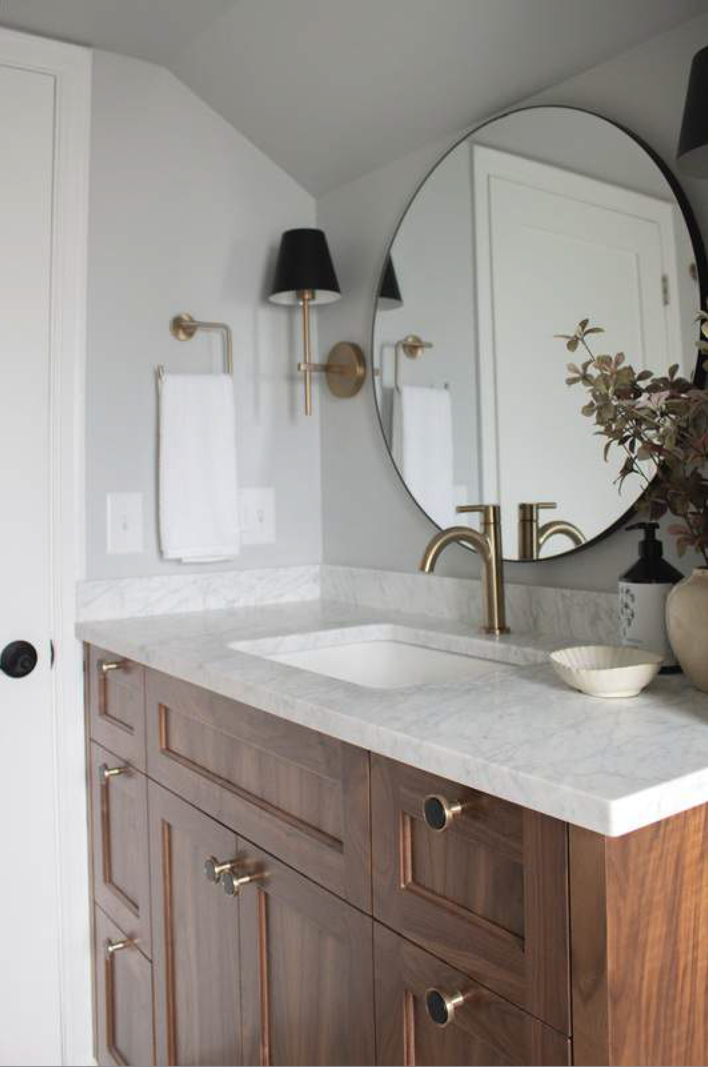 Bathroom vanity with wooden cabinet, gold hardware, round mirror, and gray walls.