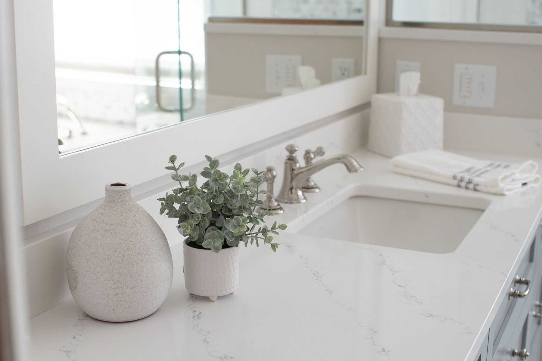 A Bathroom with A Sink , Mirror , Vase and Plant.