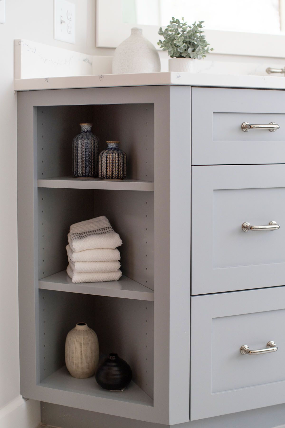 A Bathroom Vanity with A Shelf Filled with Towels and Vases.