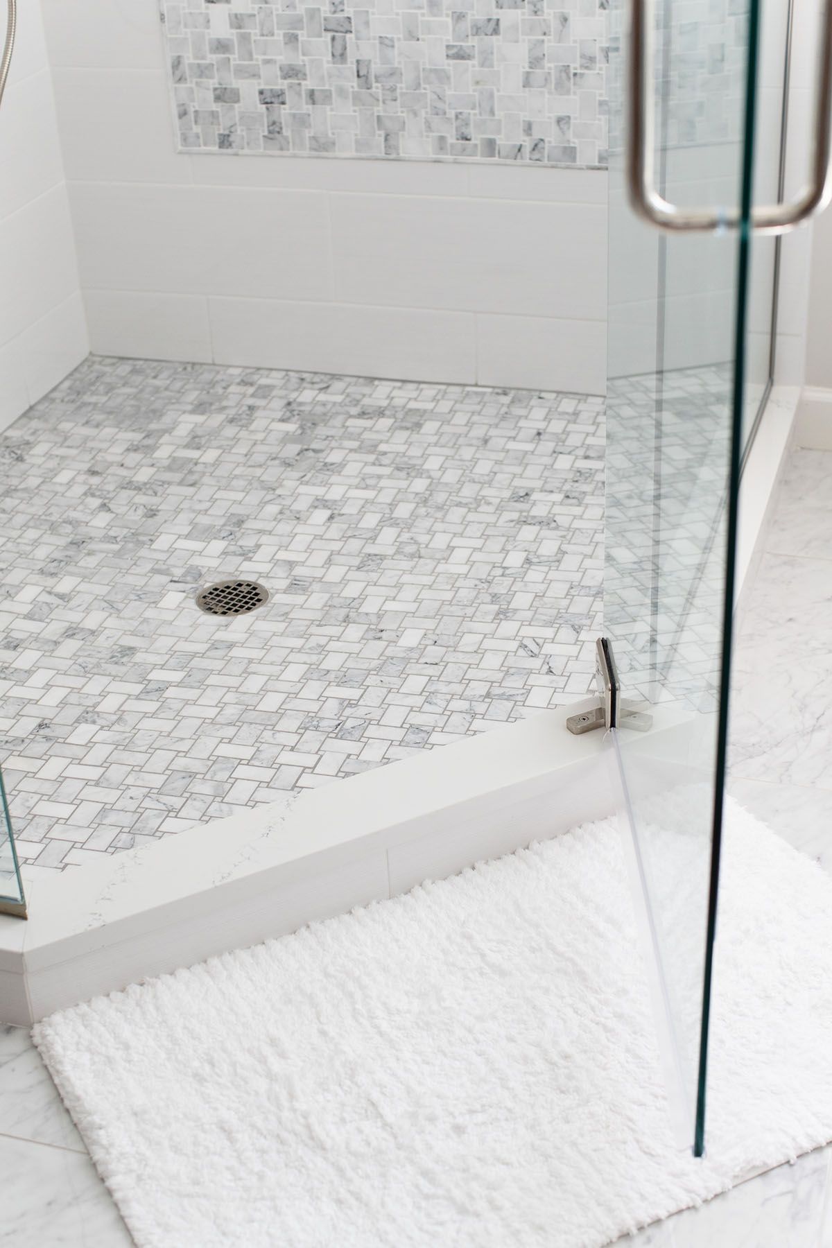 A Bathroom with A Walk in Shower and A White Rug on The Floor.