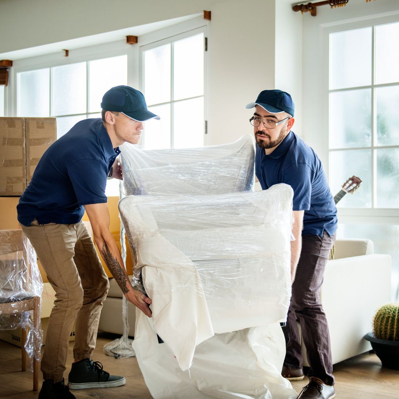 two men are carrying a large piece of furniture wrapped in plastic .