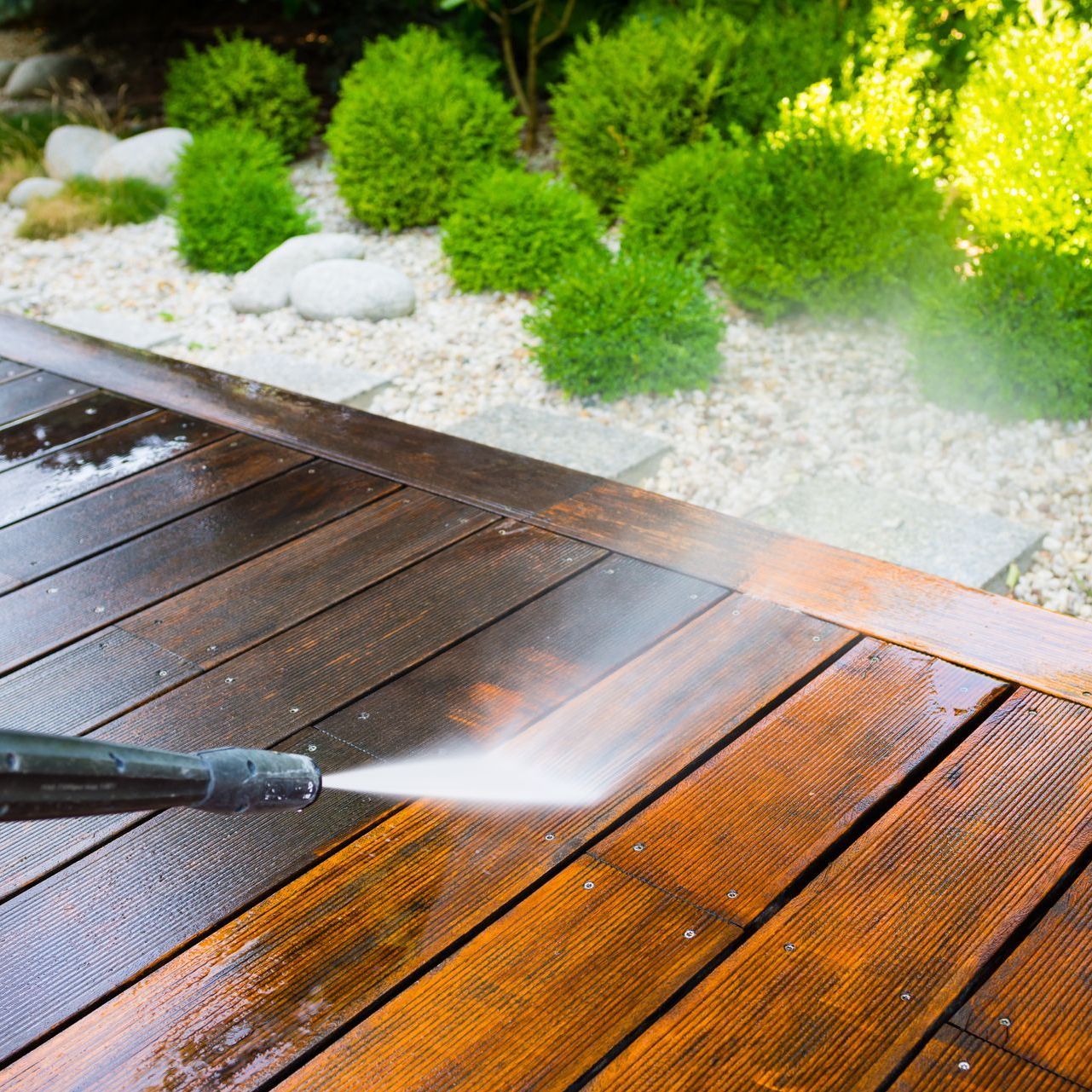 A person is using a high pressure washer to clean a wooden deck.