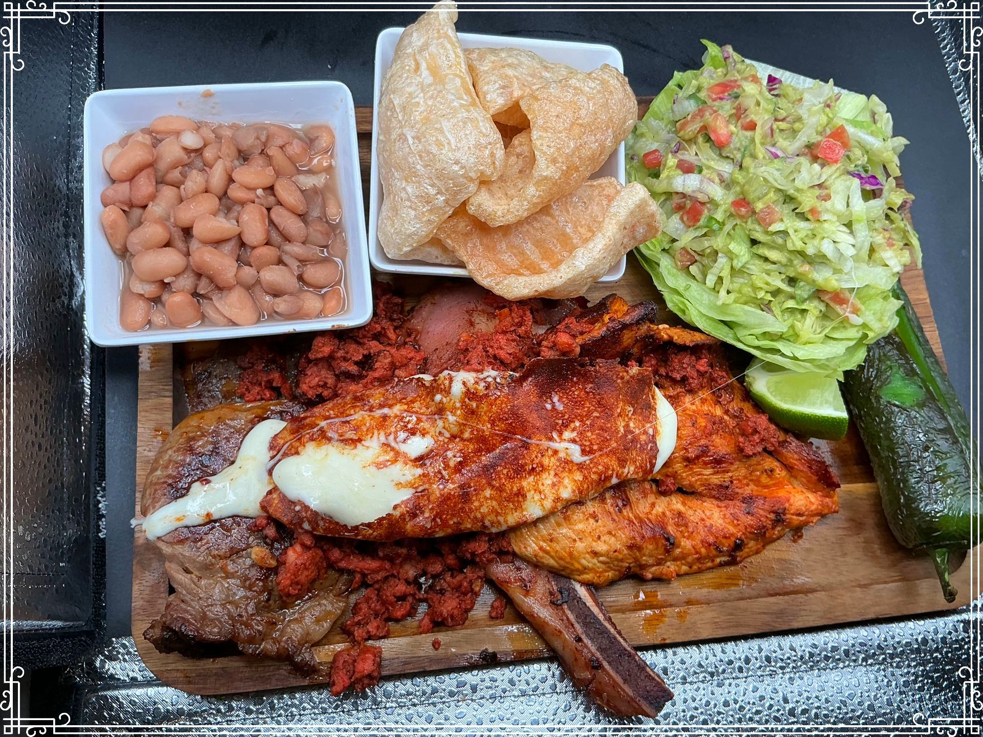 Plate of Mexican food: beans, chicharrones, guacamole, chicken, chorizo, a pepper, and a lime.