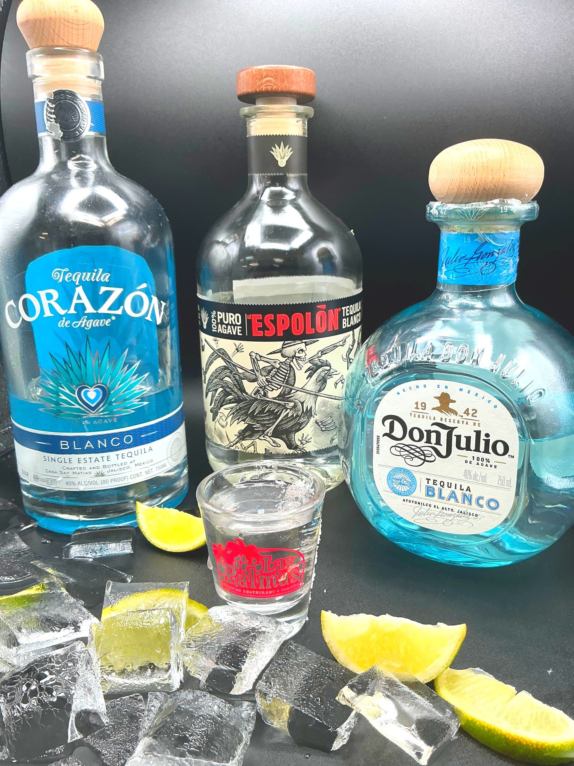 Three tequila bottles with lime wedges, ice, and a shot glass.
