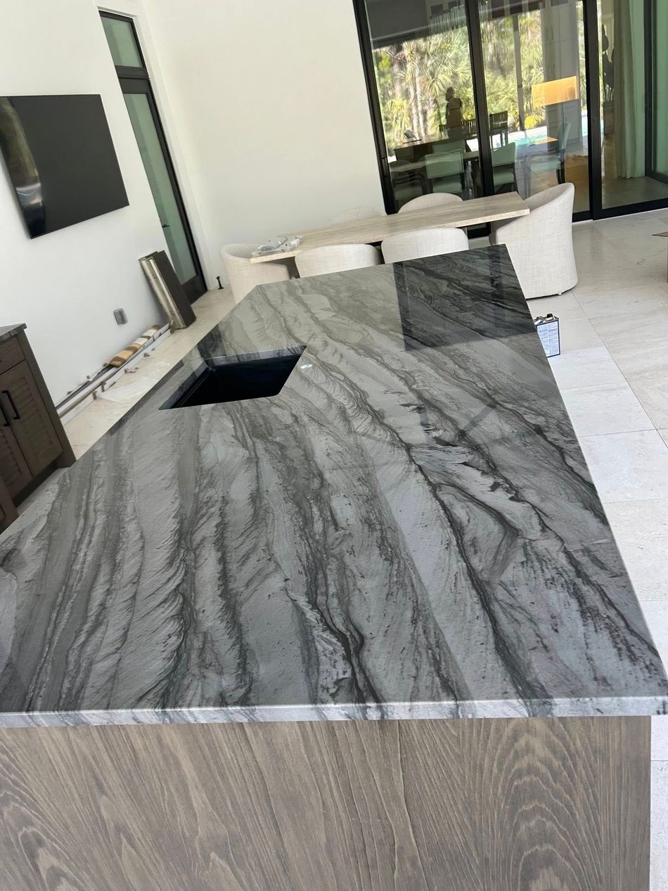 Modern kitchen island with gray marble countertop and black sink in a bright open living space.