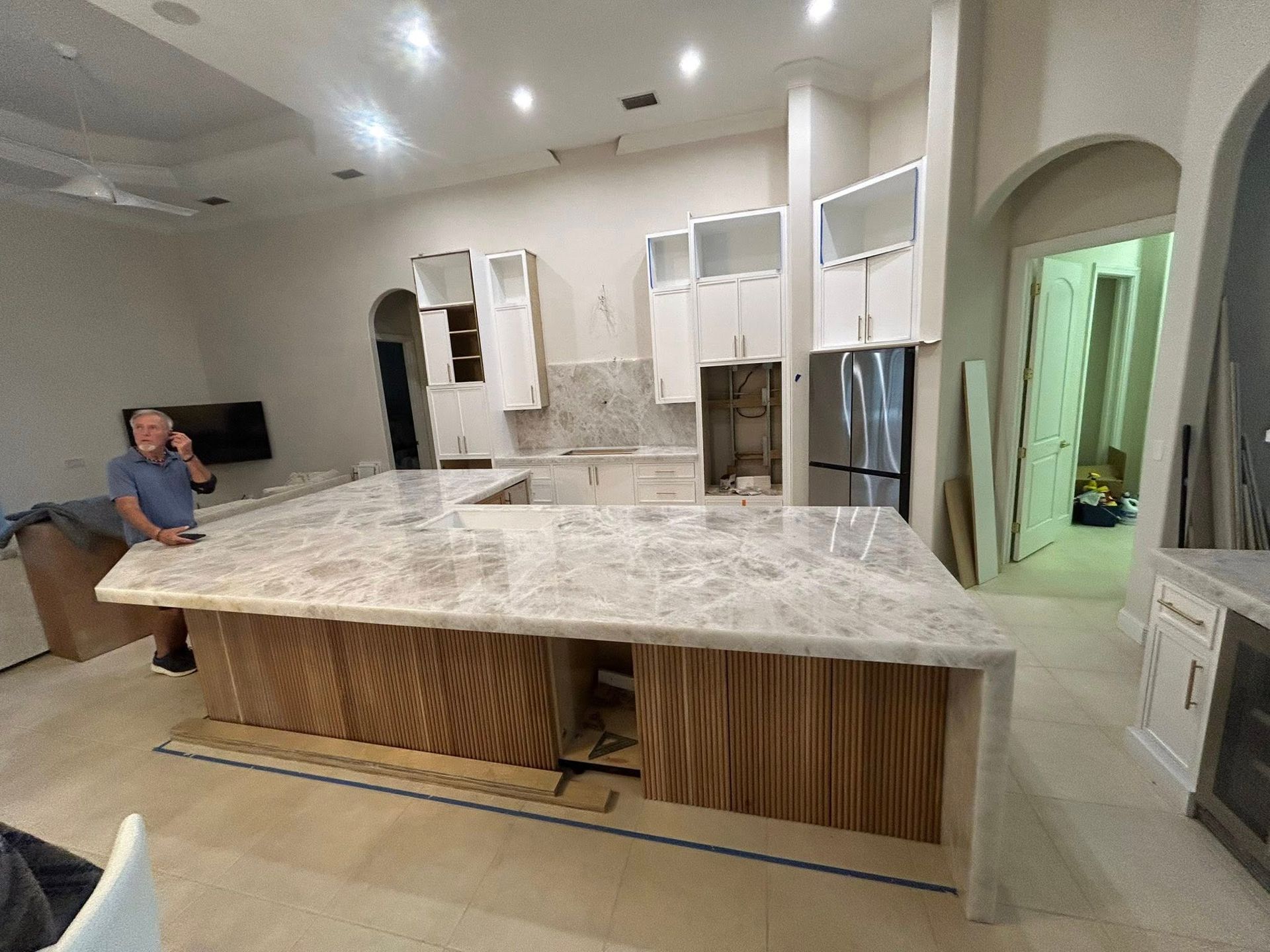 Modern kitchen under construction with a large marble island and a person working at the left side.