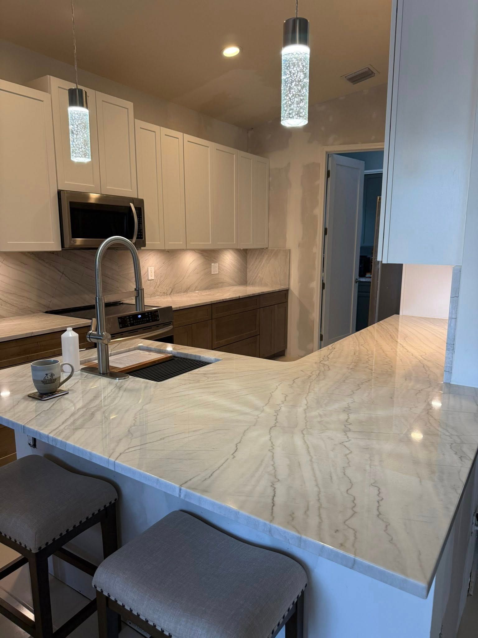 Modern white kitchen with marble island, pendant lights, and bar stools