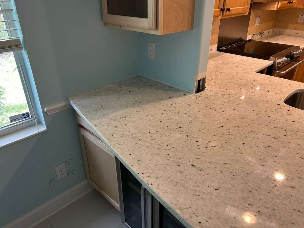 Small kitchen with blue walls and white speckled countertops, showing a corner sink area and pass-through opening.