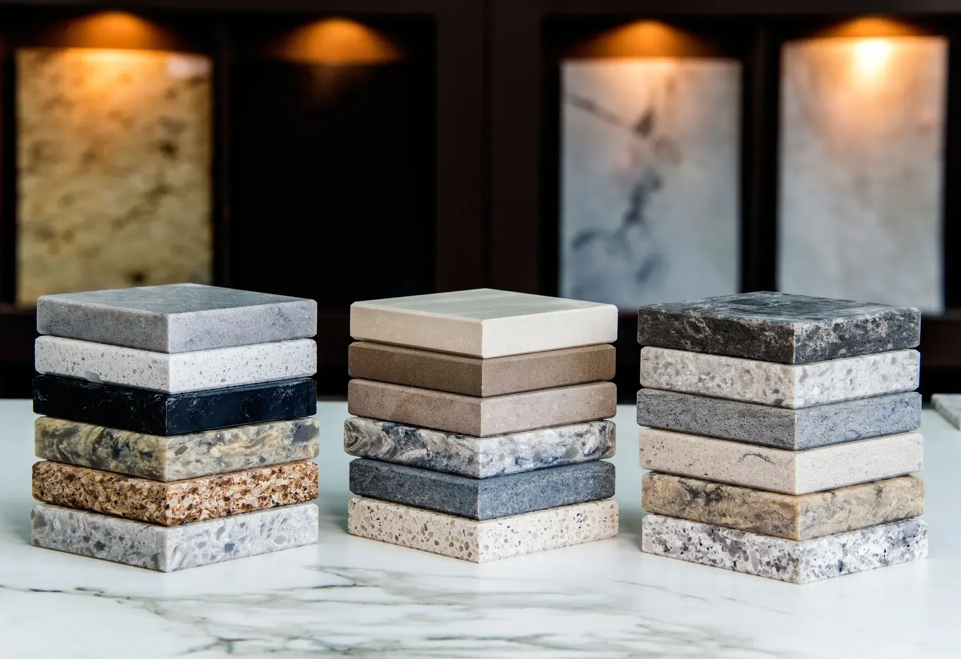 Three stacks of assorted stone tiles in shades of gray, beige, and black on a countertop