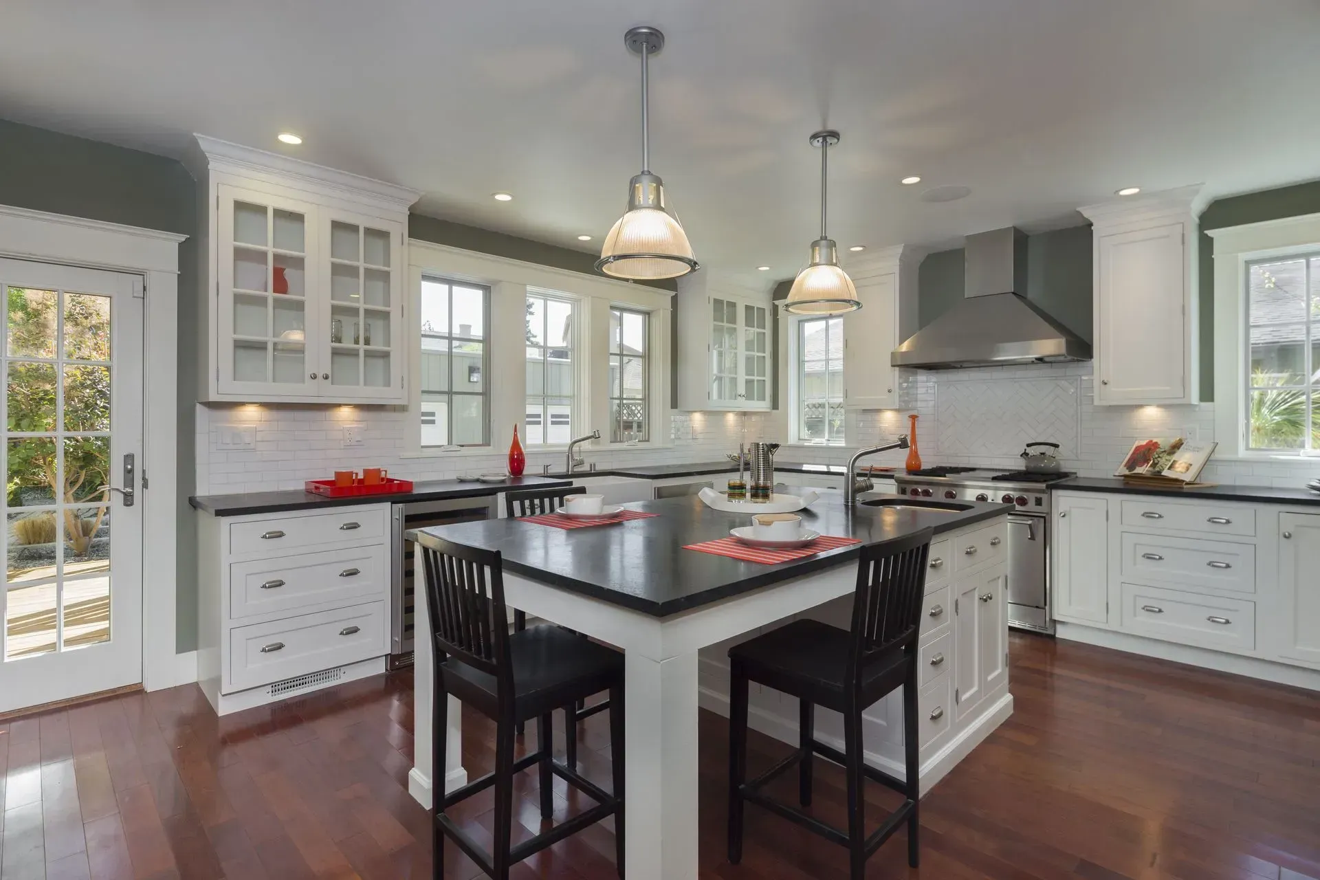Bright modern kitchen with white cabinets, dark island, pendant lights, and hardwood floors