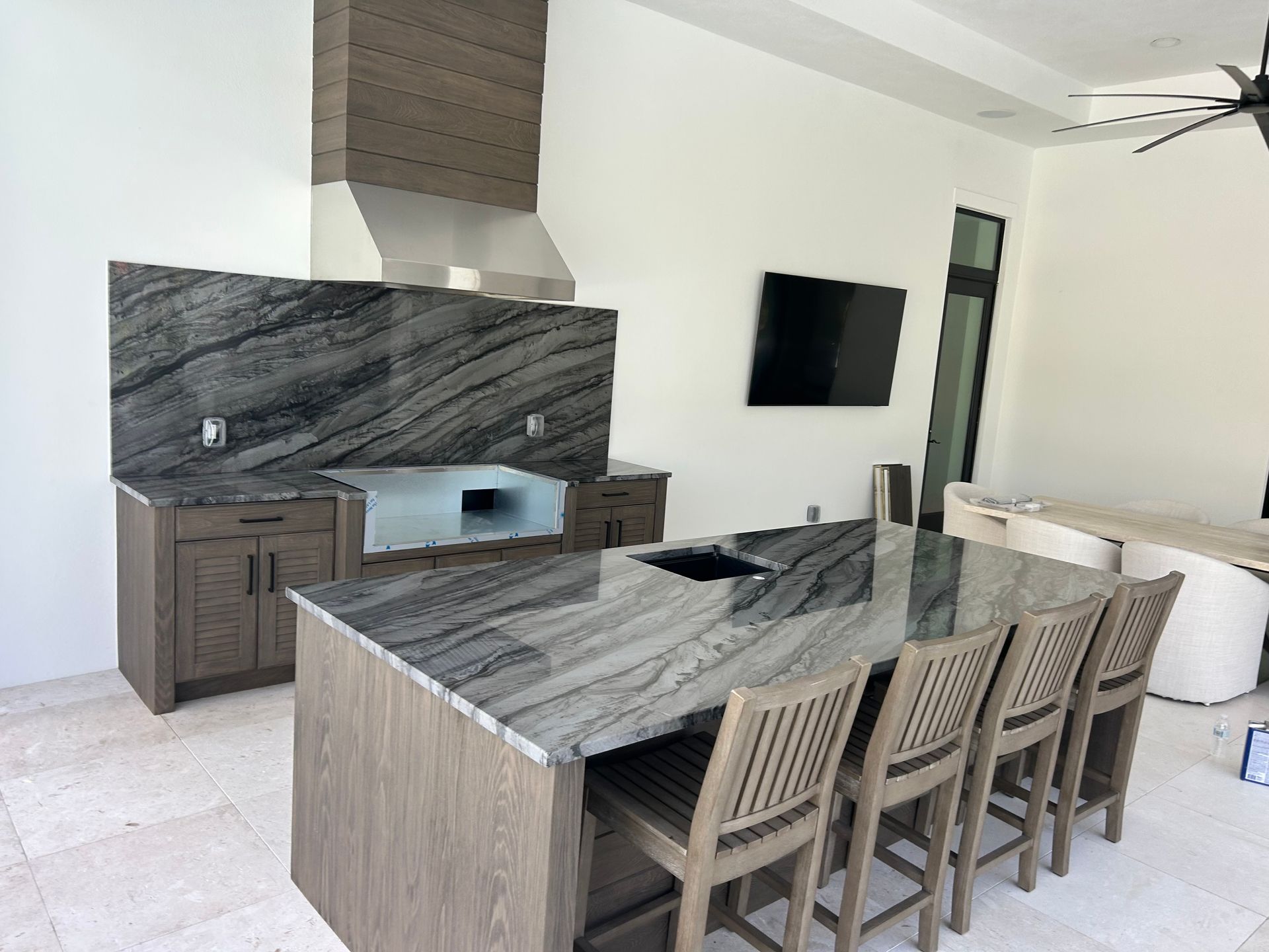 Modern kitchen with marble island, wood cabinets, stainless hood, and wall-mounted TV