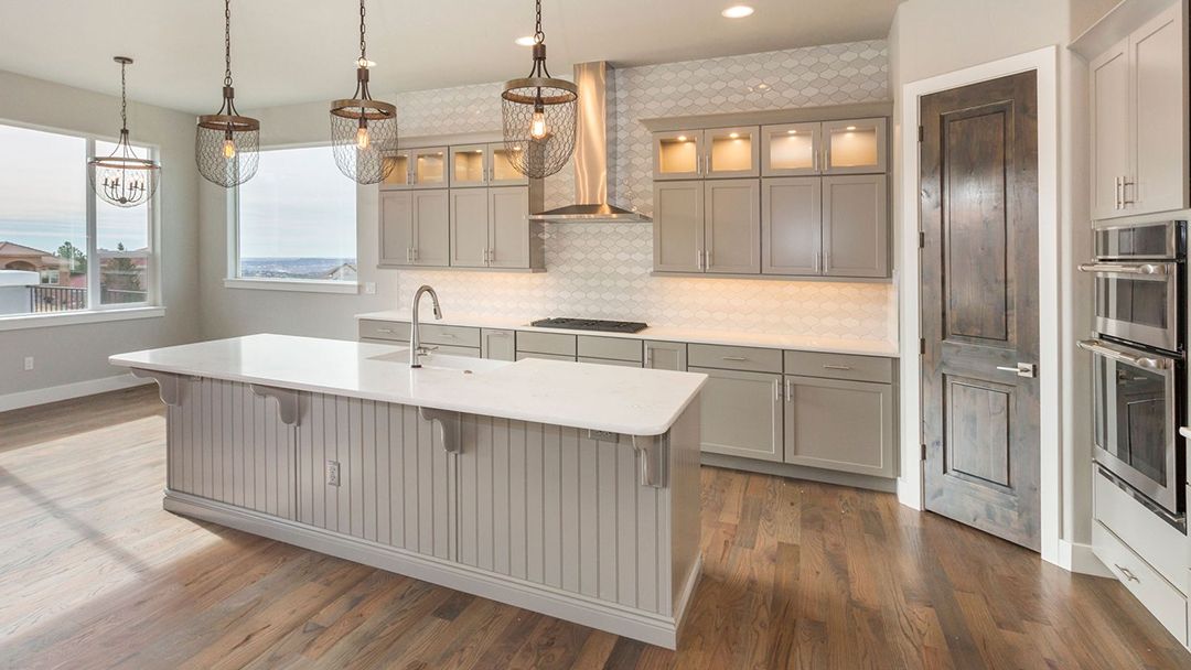 Modern bright kitchen with white island, pendant lights, wood floors, and stainless steel appliances