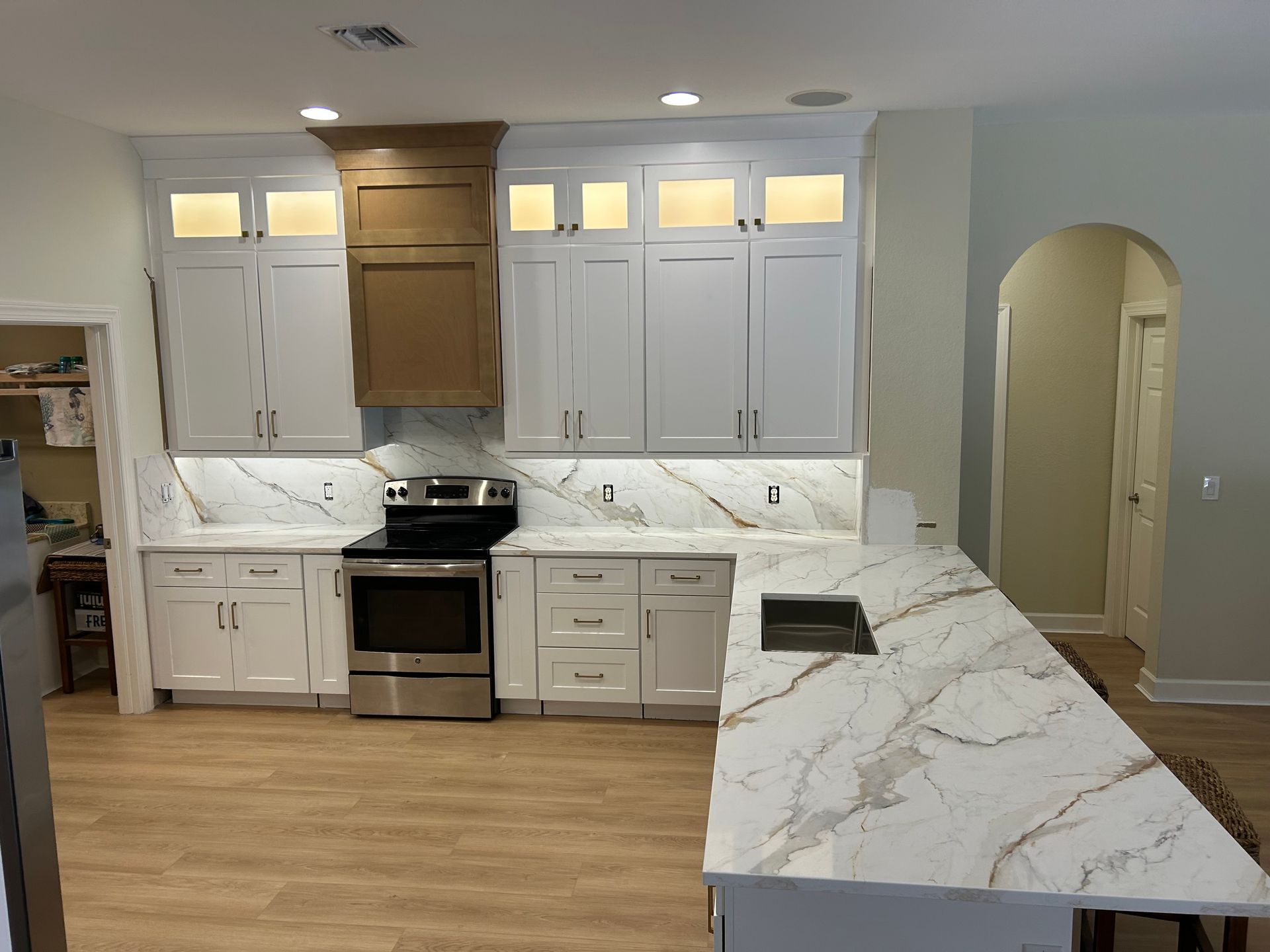 Modern white kitchen with marble countertops, stainless stove, and light wood flooring