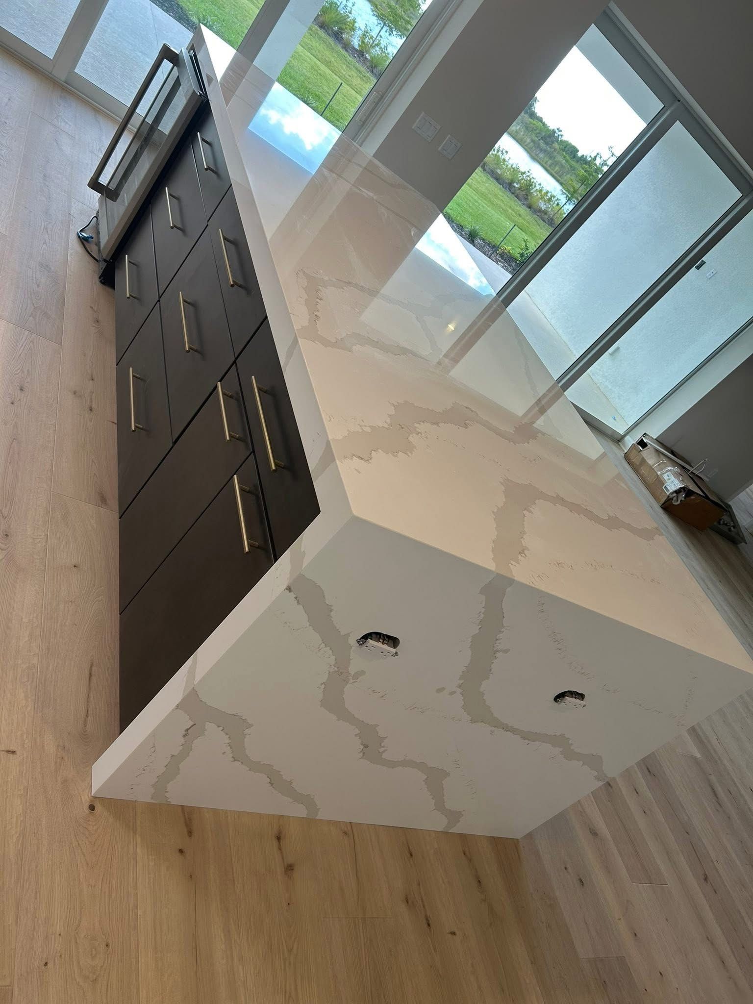 Modern kitchen island with dark cabinets, white marble-look countertop, and light wood flooring