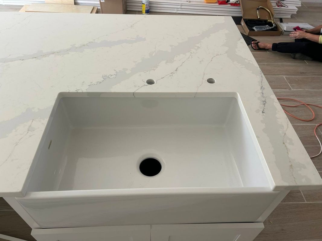 White rectangular sink basin in a marble countertop with faucet holes and a central drain, under installation.