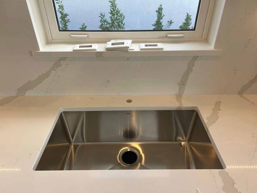 Modern kitchen sink beneath a skylight, with a stainless steel basin and unfinished countertop edges