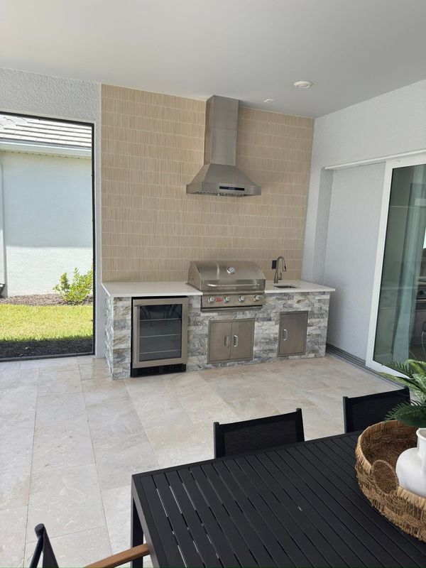 Outdoor patio with built-in stainless grill, mini fridge, and tiled counter beside a sliding glass door