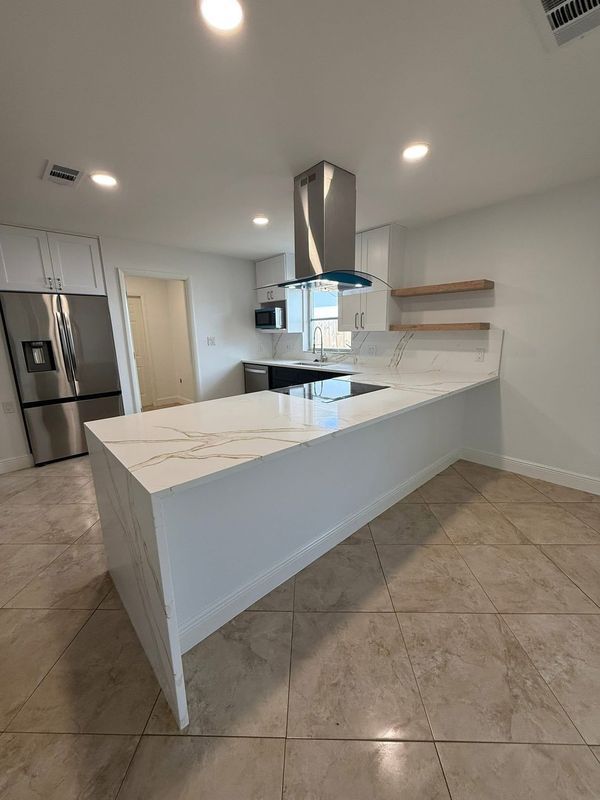Modern white kitchen with marble island, stainless appliances, and beige tile floor