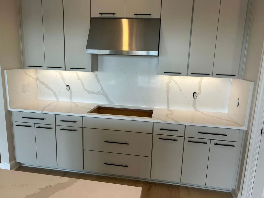 Modern kitchen with white cabinets, stainless hood, and marble backsplash under bright lighting
