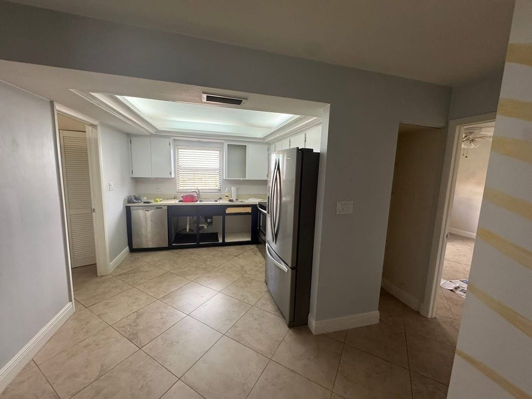 Empty kitchen and dining area with beige tile floor, white cabinets, and stainless steel appliances.