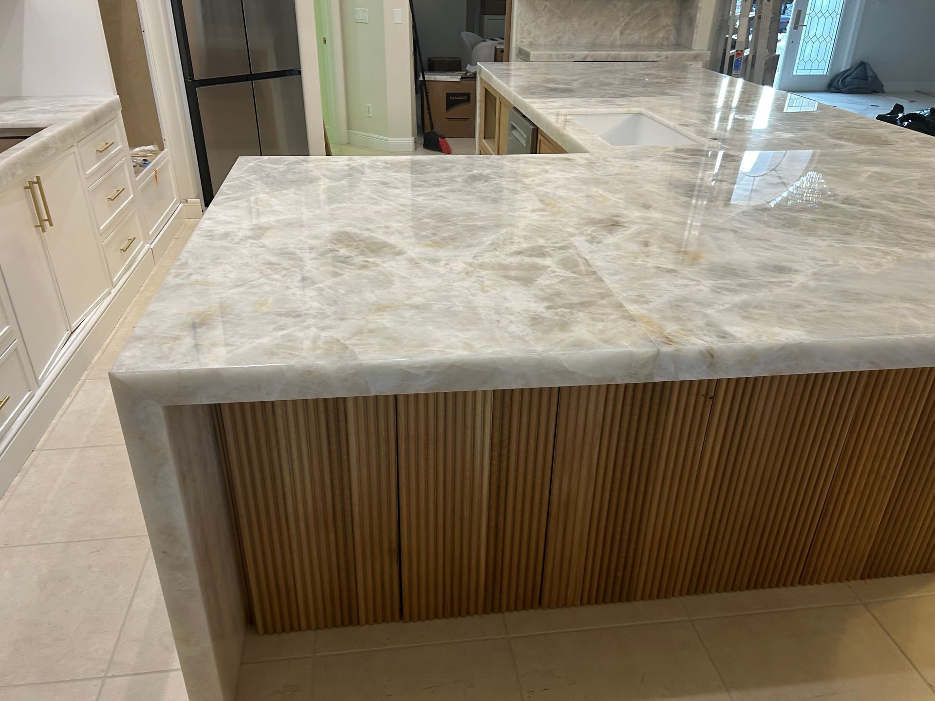 Modern kitchen island with white marble countertop and vertical wood slat front in a bright tiled room