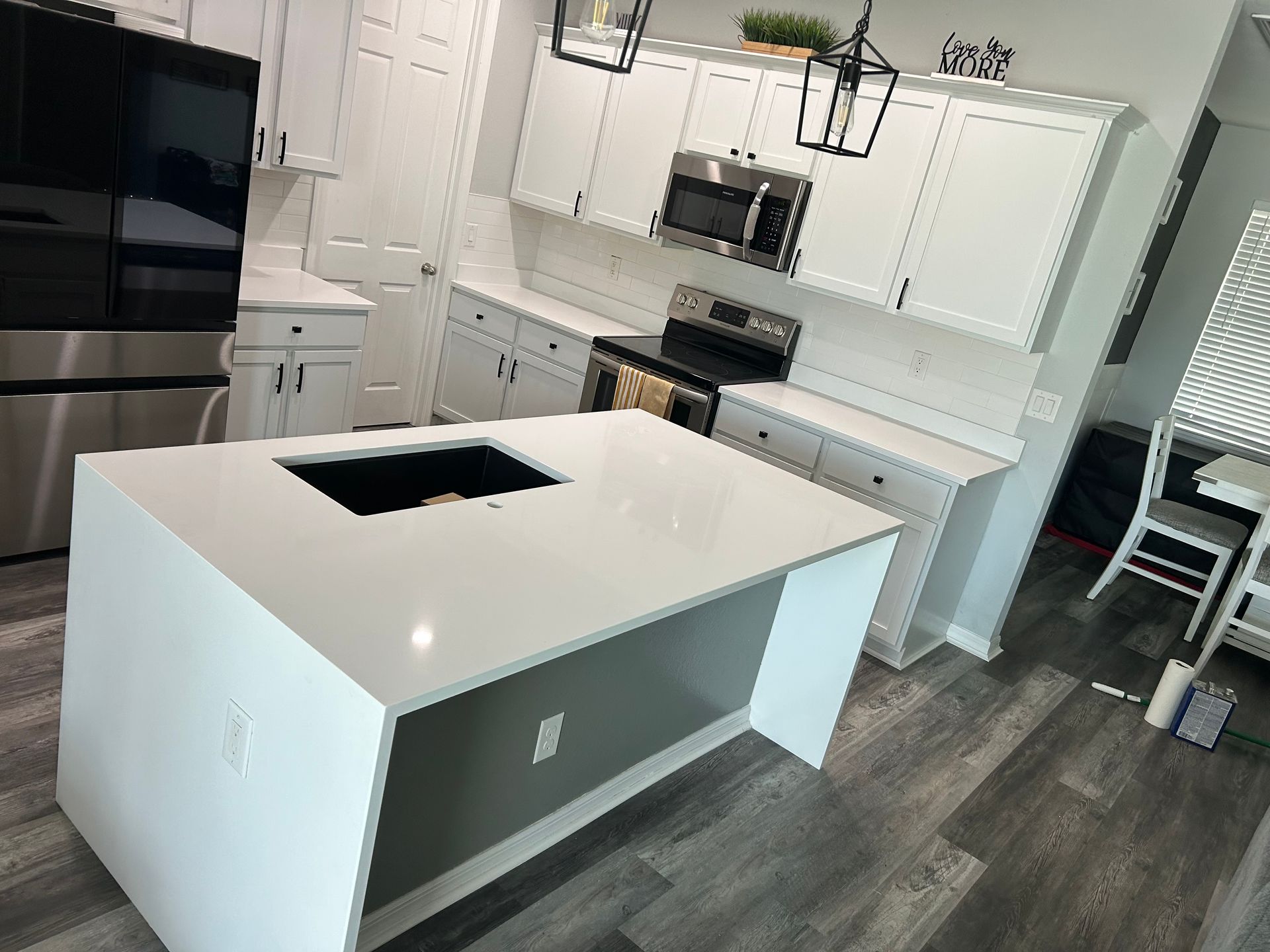 Modern kitchen with white cabinets, gray floor, and a white island with a black cooktop opening