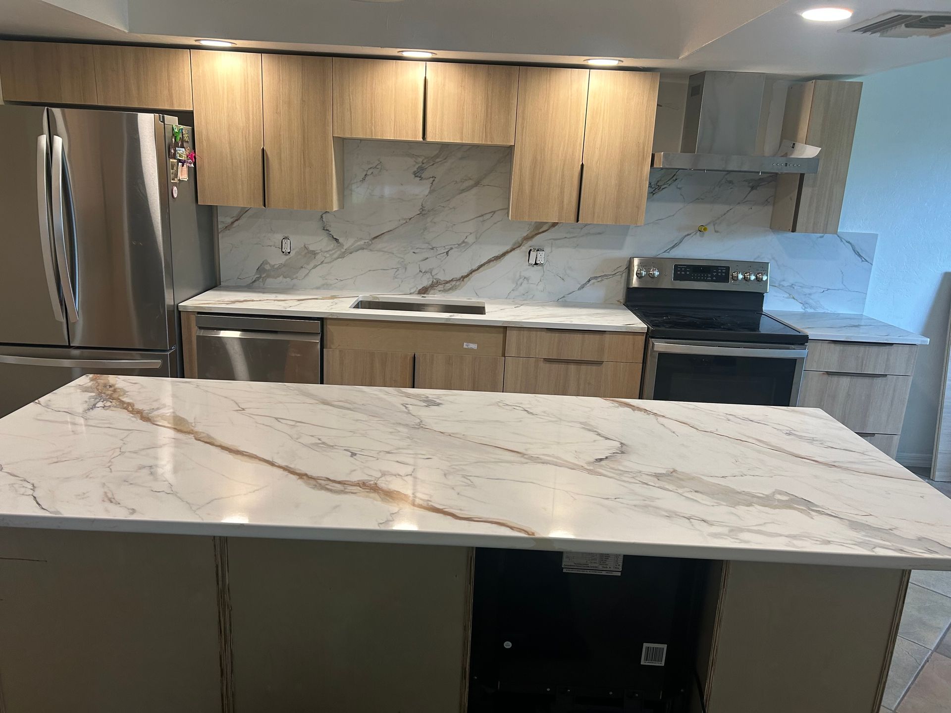 Modern kitchen with wood cabinets, marble counters, stainless appliances, and a large island.