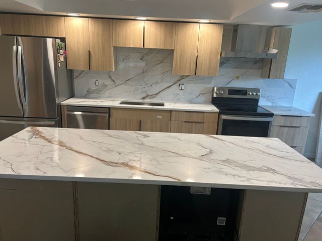Modern kitchen with wood cabinets, marble countertops, stainless steel appliances, and a large island.
