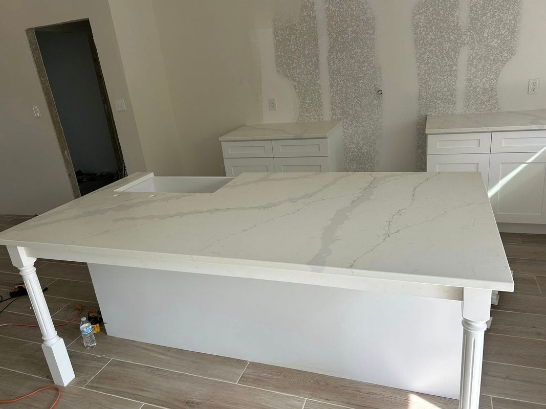 White marble dining table with white legs in a bare room, beside a mirror and two white nightstands.