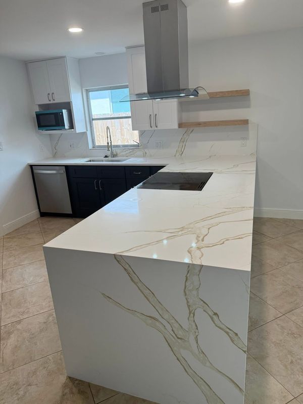 Modern white kitchen with marble island, black cabinets, stainless appliances, and tiled floor.