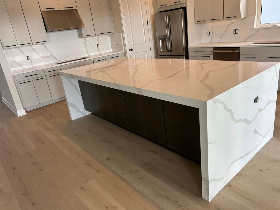 Bright modern kitchen with a large white island, light wood floors, and stainless steel appliances
