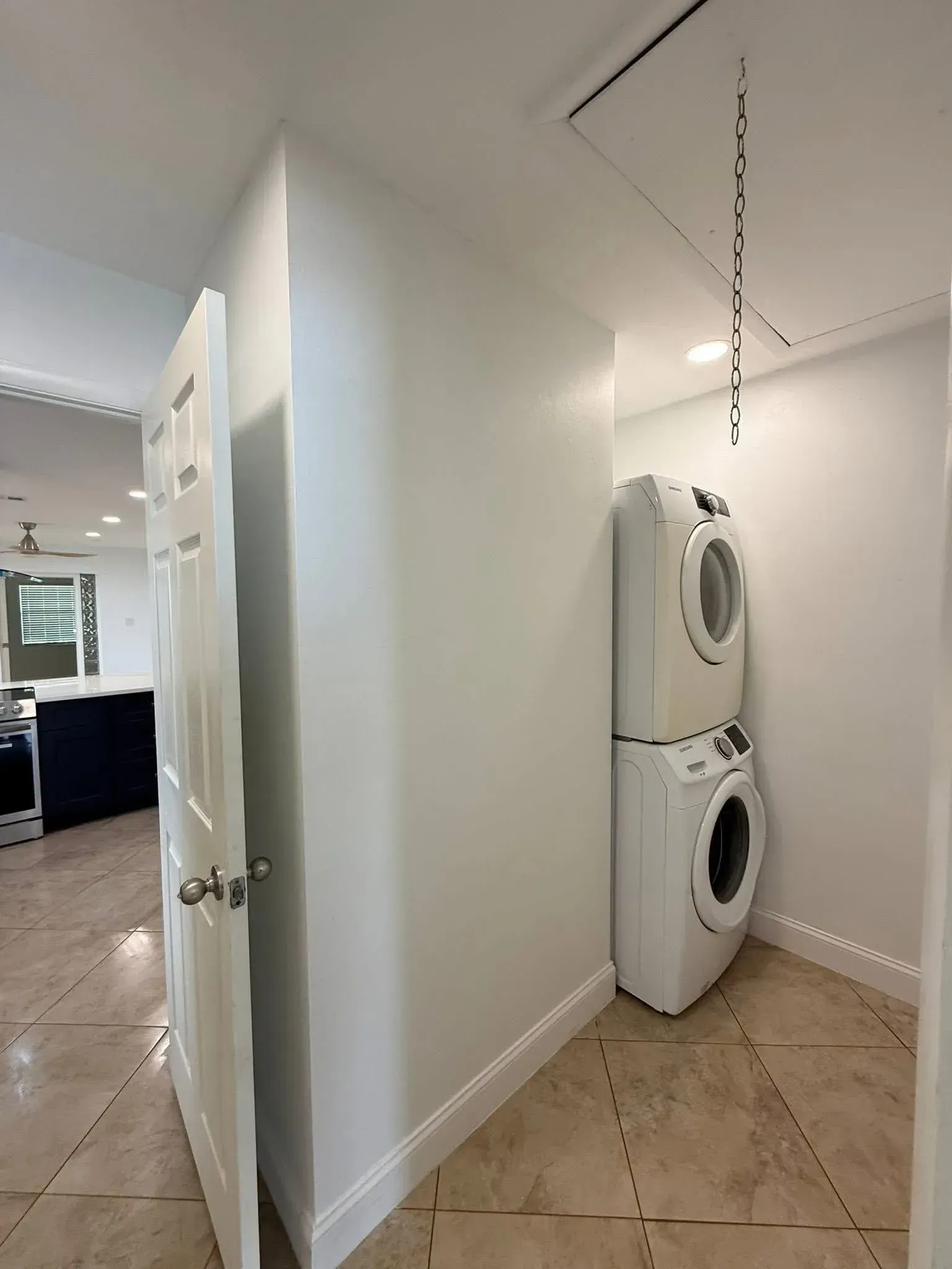 Narrow hallway with stacked washer and dryer beside a white wall and tiled floor.