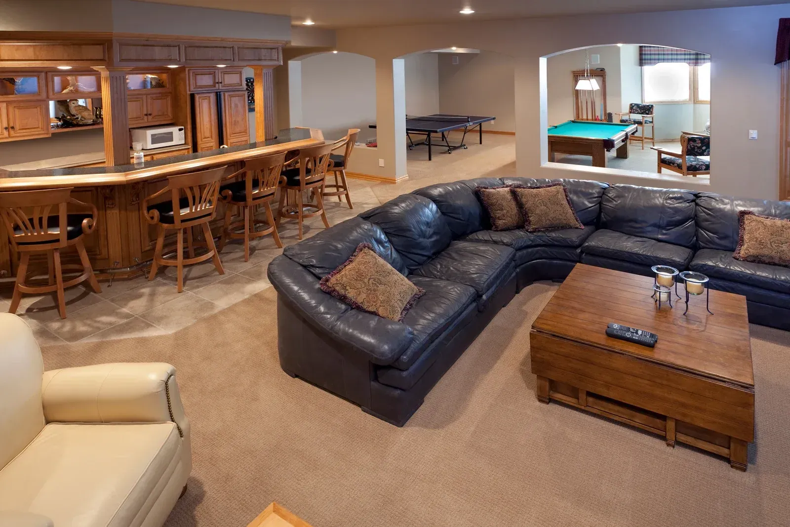 Spacious basement lounge with dark blue sectional, pool table, bar, and seating area