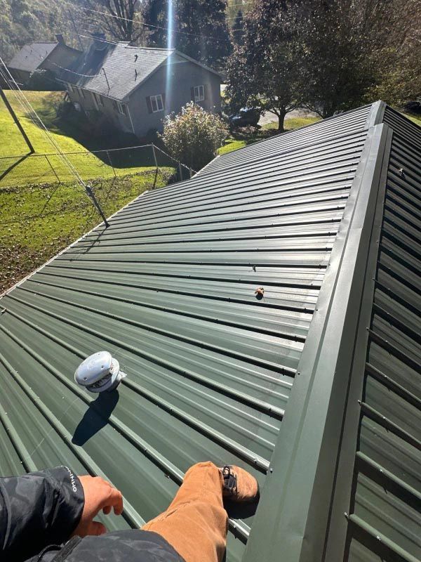 A person is sitting on top of a green metal roof.