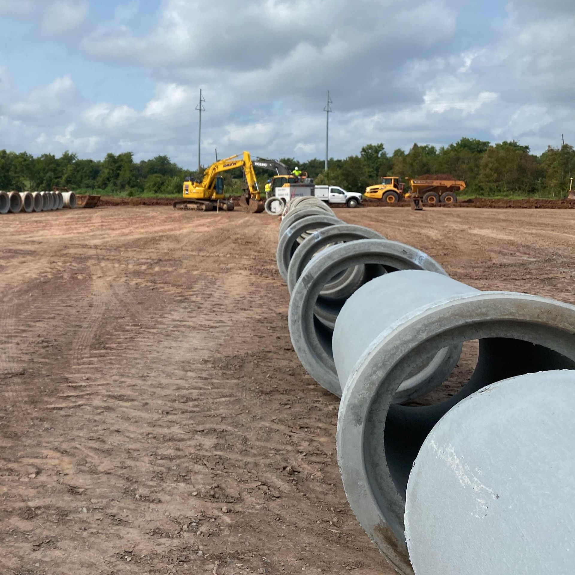 A row of concrete pipes are lined up in a dirt field