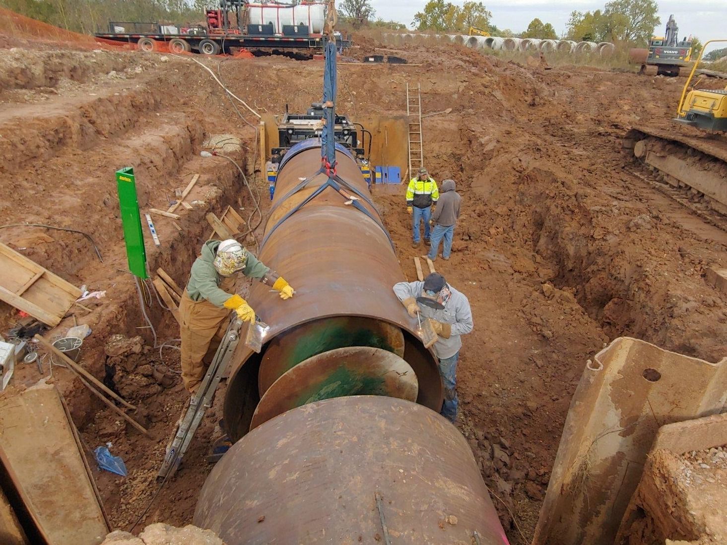 A group of men are working on a large pipe in the dirt.