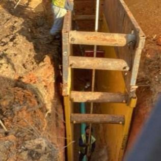 A man is standing in a trench with a ladder.