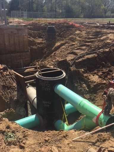 Green pipes are being installed in a hole in the ground