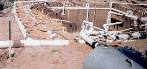 A bunch of pipes are laying on the ground next to a tank.