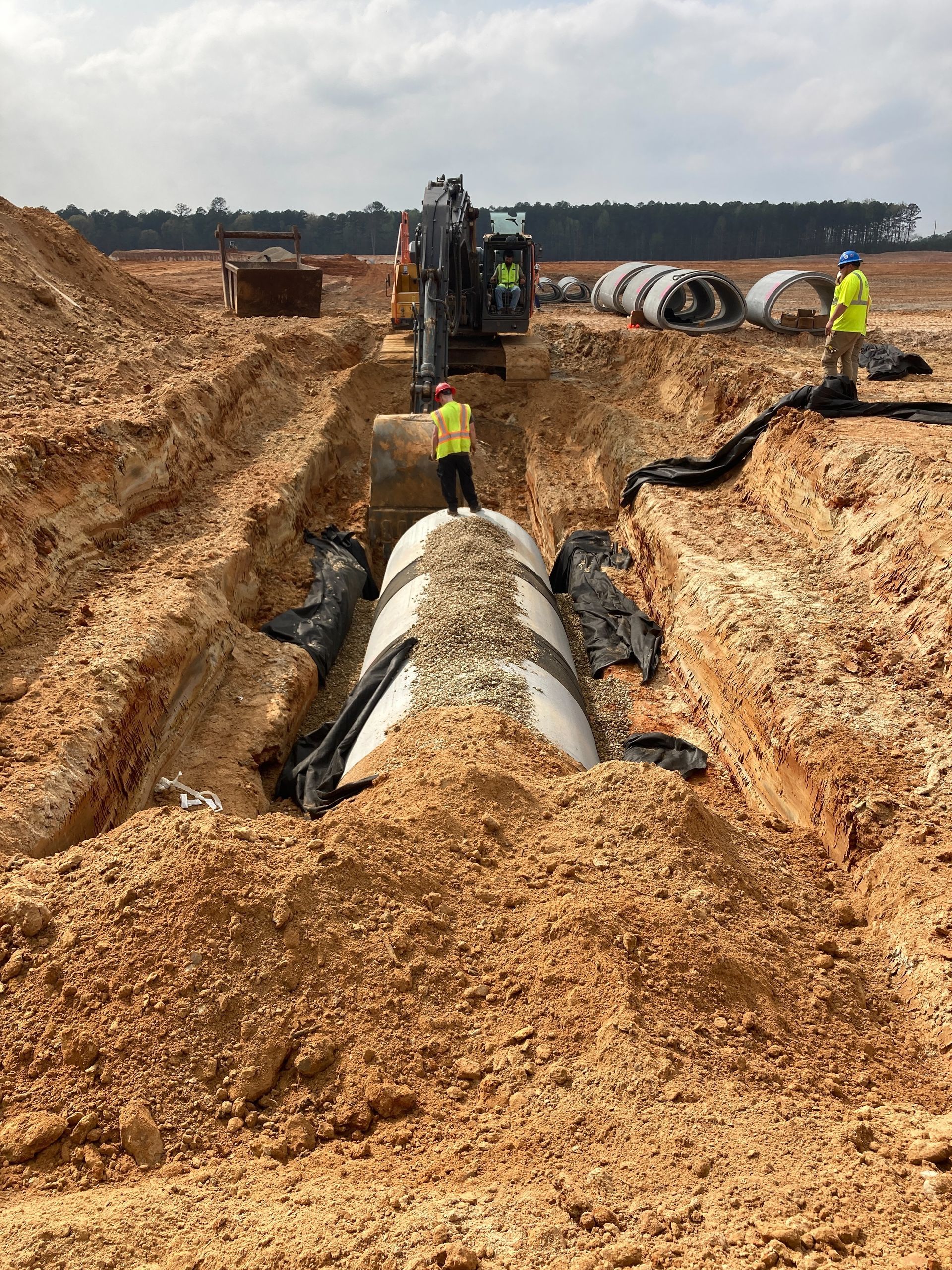 A group of construction workers are working on a large pipe in the dirt.
