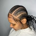 A person with their hair styled in neat, tight cornrows pulled back into a curly ponytail, with thin loose strands in front.