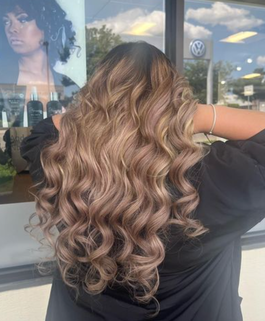 A woman with long curly hair is standing in front of a window.