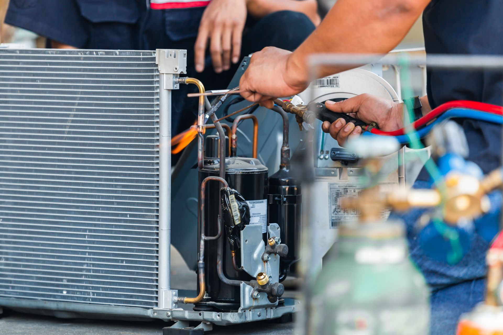 Technicians repairing an HVAC unit, with tools and hoses attached to the open system.